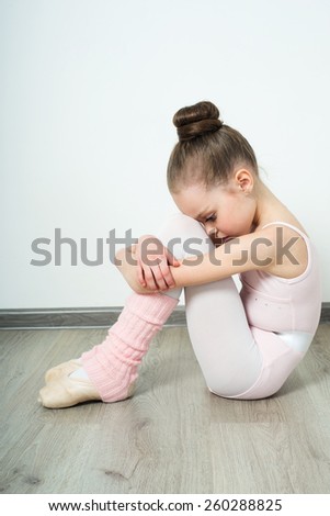 A little adorable young ballerina does ballet poses and stretching exercises on the floor at home