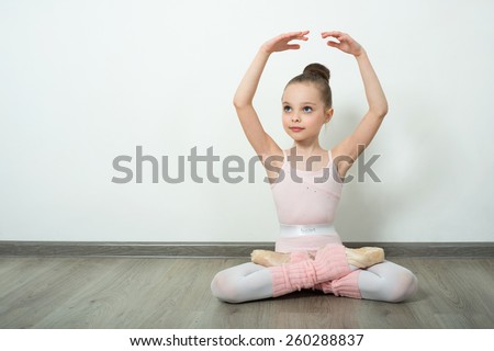 A little adorable young ballerina does ballet poses and stretching exercises on the floor at home