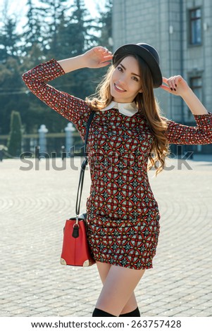 Beautiful brunette girl in stylish dress jumps on the city square. Fashion and city style. Facial expression.