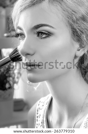 Make-up artist applying foundation powder or blush with makeup brush on model\'s cheeck, close up. Black and white