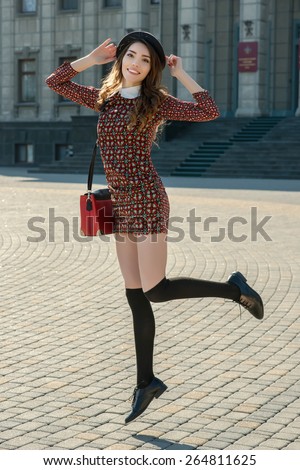 Beautiful brunette girl in stylish dress posing on the city square. Fashion and city style. Facial expression. Various flags and the Orthodox Church on background.