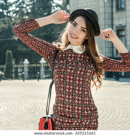 Beautiful brunette girl in stylish dress posing on the city square. Fashion and city style. Facial expression