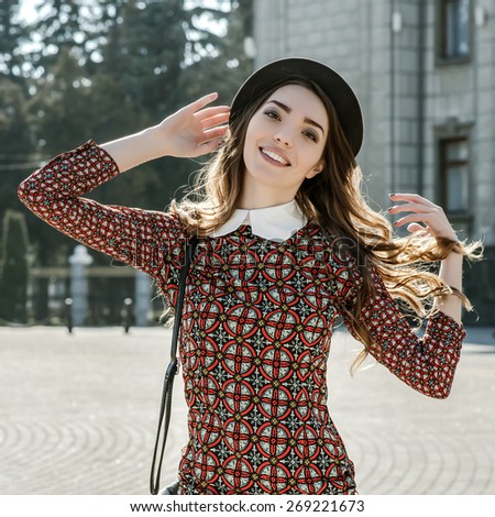 Beautiful brunette girl in stylish dress posing on the city square. Fashion and city style. Facial expression