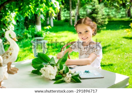 Little smiling girl  writing on notebook outdoor in the park. Vintage style. Facial expression.