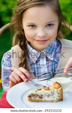 Cute smiling little girl sitting by dinner table and eating cake. Kid eats healthy food. Fine dinning.