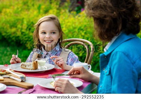 Cute smiling little girl sitting by dinner table and eating cake. Kid eats healthy food. Fine dinning.