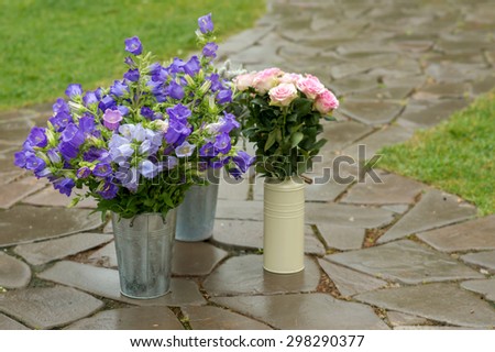 Buckets and cans with flowers outdoor. Blue bells and pink rose. Bouquet of flowers. Gardening. Selective focus, close up.