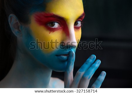 Painted beautiful woman face, artistic make up, body and face art, close up. Facial expression, emotions. Bird Halloween  beauty fashion style in red, yellow, blue colors. Halloween