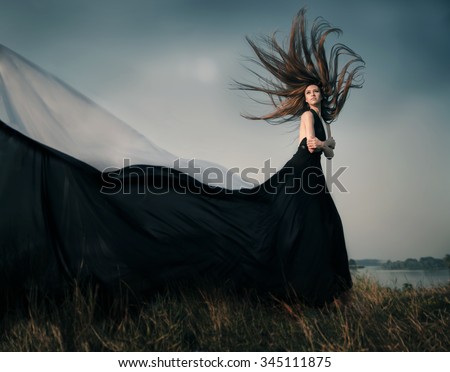 Fashion female model with long blowing hair outdoor. Portrait of sexy glamour woman with healthy and beauty flying fluttering long brown hair  wearing  black dress resists strong wind. Copy space.