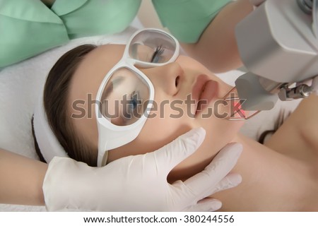 Therapist beautician makes a  laser rejuvenation for the model by  apparatus  in a beauty salon.  Close up, selective focus.