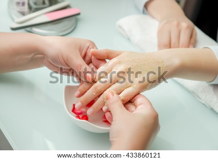 Woman hands receiving a  hand scrub peeling by a beautician in beauty salon. SPA manicure, hand massage  and body care. Close up, shallow dof.