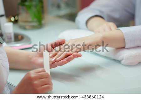 Woman hands receiving a manicure in beauty salon.  Nail filing. Close up, selective focus.