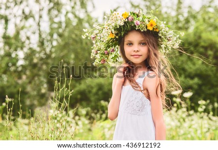 Cute smiling little girl with flower wreath on the meadow at the farm. Portrait of adorable small kid outdoors. Midsummer.