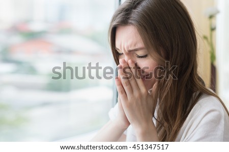 Young sad woman sits alone front of the window. Crying girl. Allergy, illness, depression, stress concept.