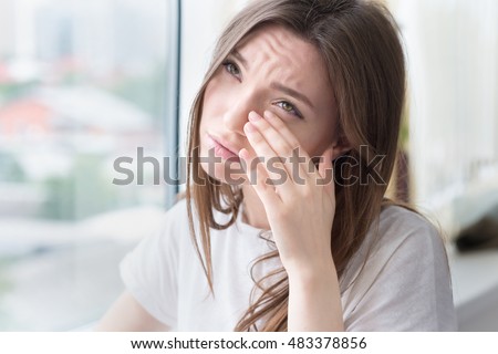 Young sad woman sits alone front of the window. Crying girl. Allergy, illness, depression, stress concept.