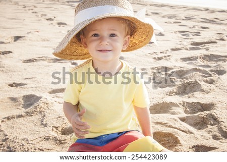 a cute little boy playing on the beach in the sand with mom's summer hat