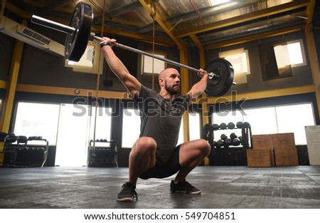 strong crossfit athlete in a heavy overhead squat lift in a cross-fit box gym