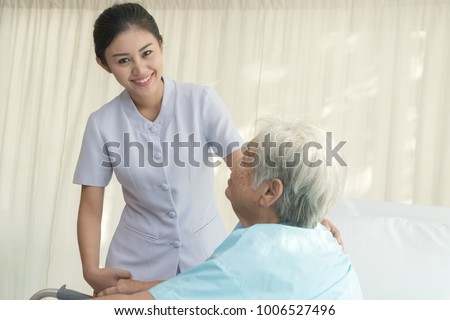 Cheerful asian nurse visiting elderly patient to check up after surgery in hospital for giving physical therapy and encouragement.