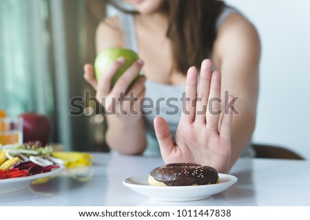 Woman on dieting for good health concept. Close up female using hand push out her favourite donut and choose green apple and vegetables for good health.
