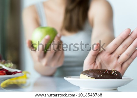 Woman dieting for good health concept. Close up female using hand push out her favourite donut and choose green apple and vegetables for good health.