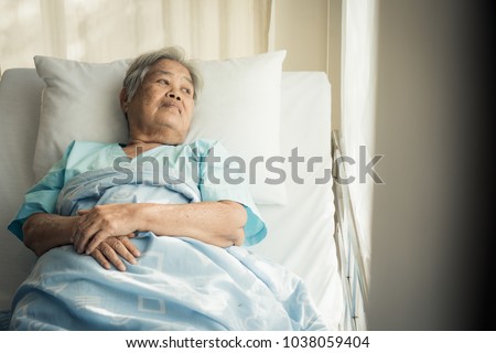 lonely asian elderly female patient lying on the bed in the hospital and looking away outside the window waiting to see her child and her family to visit.