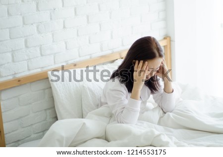 Asian women are headache severely.Lady wake up in the morning with migraine.Insomnia results in headaches when awakened.Young girl sitting on a stressed bed. In her bedroom.She was sick.