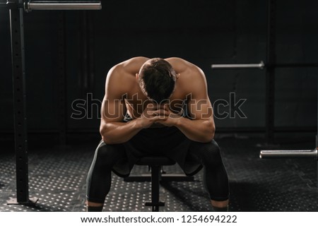 Strong sporty man sitting on gym bench suffering breakdown to overcome. Demotivation sport concept. Cross fit training
