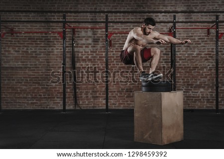 Crossfit athlete doing box jump exercise at the gym. Man practicing functional training. Copy space