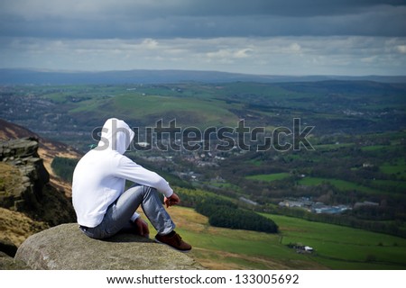 man with hood sitting on cliff and looking to a view