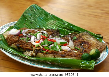 BBQ stingray on banana leaf garnished with spring onions, onions, red chillies and lime on a plate