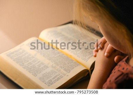 Hands of a little girl in prayer. The little girl prays in the evening. A girl with a bible.