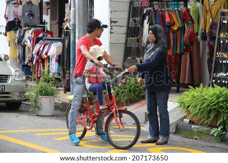 GEORGE TOWN, MALAYSIA - MAY 30: A typical Malay couple with their child on a bicycle outside a shop in a street of George Town, Malaysia on the 30th May, 2014.