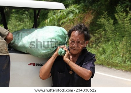 MAE SOT, THAILAND - SEPTEMBER 1: A hill tribe man unloading a heavy bag from the back of a car on the highway from Mae Sariang heading south to Mae Sot, Thailand on the 1st September, 2014.
