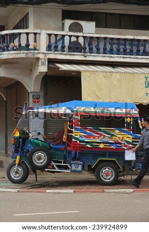 VIENTIANE, LAOS - AUGUST 6: A local man walking past a colorful tuk tuk parked on the side of the road in Vientiane, Laos on the 6th August, 2014.