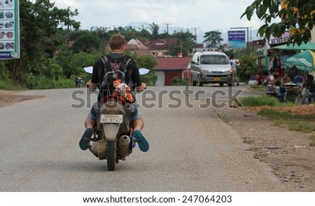 VANG VIENG, LAOS - AUGUST 11: The back view of a tourist on a motorbike with a funny soft toy in the town of Vang Vieng, Laos on the 11th August, 2014.