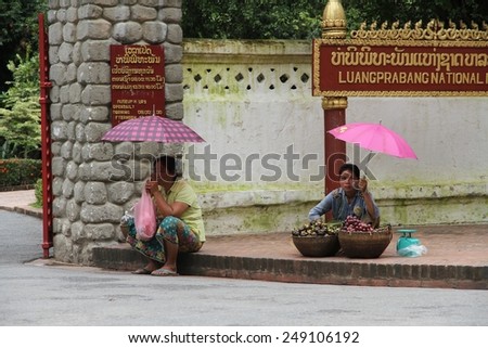 LUANG PRABANG, LAOS - AUGUST 14:\
Local hill tribe women sitting in the shade of pink umbrellas at the entrance to the Royal Museum in the Unesco town of Luang Prabang, Laos on the 14th August, 2014.
