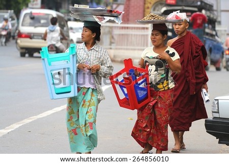 MANDALAY, MYANMAR - NOVEMBER 7: Two local women carrying stools with a monk in the background on a busy road in the town of Mandalay, Myanmar on the 7th November, 2012.