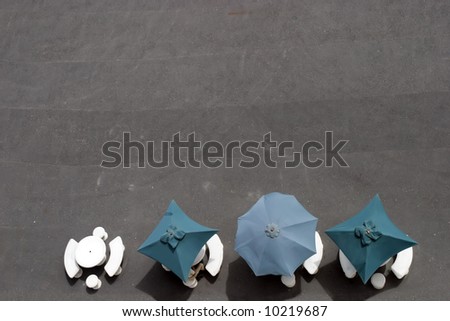 Three umbrellas, four tables and a man sitting at a outdoor cafe