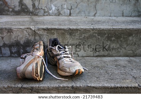 A pair of old used  running shoes on cement steps.