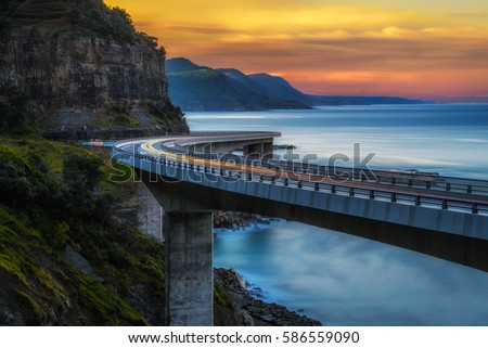 Sunset over the Sea cliff bridge along Australian Pacific ocean coast with lights of passing cars near Sydney, Australia. Long exposure.