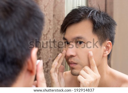 Mirror reflection of a young asian handsome man applying facial cream on face