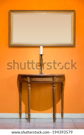 candle on candle stick and old wood table and picture frame on orange wall