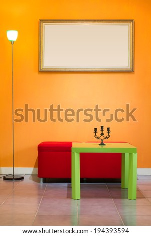 red stool chair, floor lamp, candlestick on green table and picture frame on orange wall