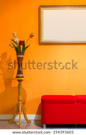 red stool chair, flowers vase on the side table and picture frame on orange wall