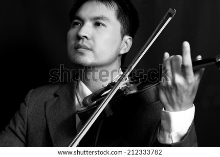 Asian handsome musician play violin on dark background, B&W film processed