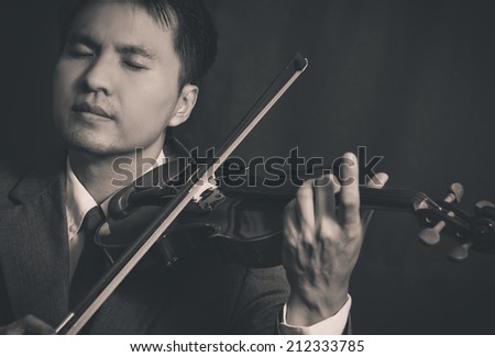 Asian handsome male musician plays violin and close his eyes on dark background , B&W old film processed