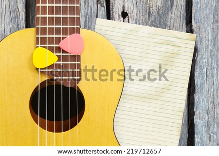 small acoustic guitar and yellow,pink picks on fingerboard close up , old blank paper on old aged wood texture background