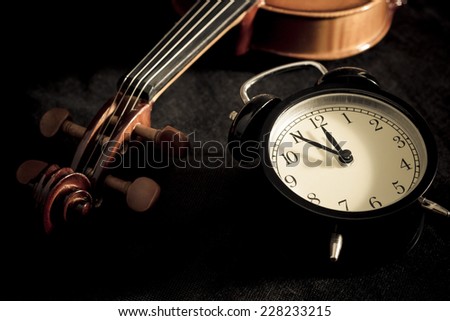 Low key image of alarm clock & old aged classical violin on black fabric /  \