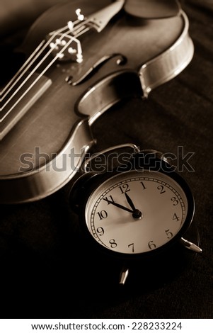 Low key image of alarm clock & old aged classical violin on black fabric , sepia film processed /  \