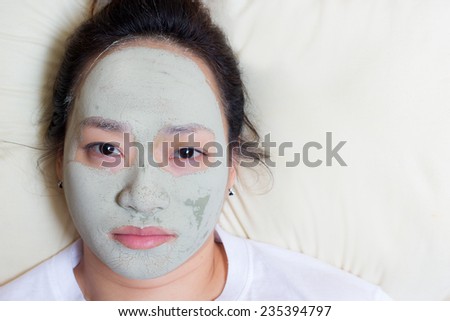 asian woman in clay mud facial mask on face on bed , Girl taking care of dry complexion. Beauty treatment